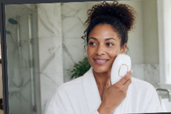 Woman in a white robe using a Lumimor IPL device in her bathroom